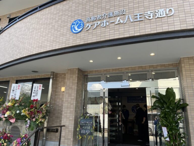 介護施設の玄関。タイル張りの建物にロゴサイン、装飾花が飾られている。